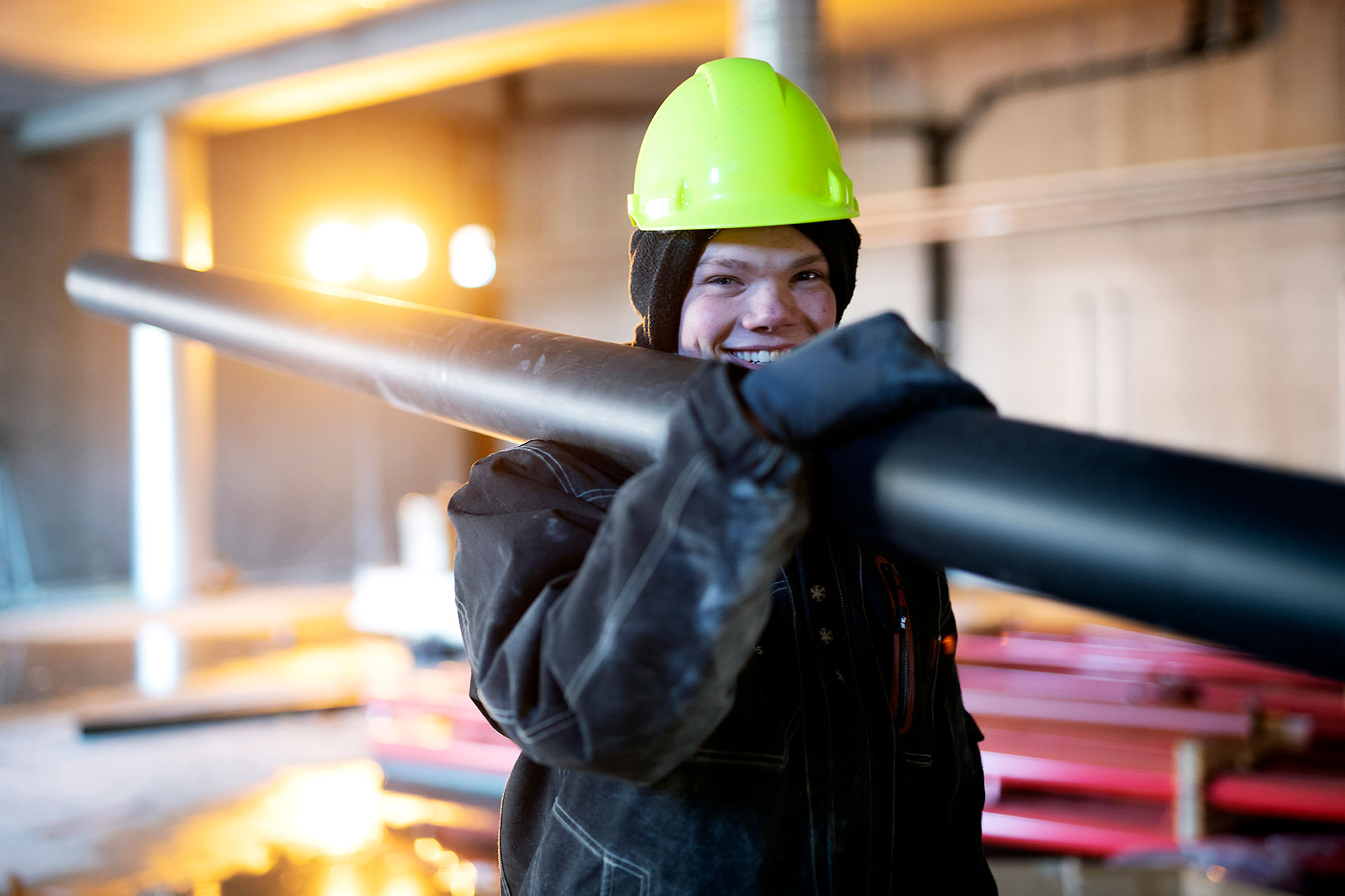 VB-rørlegger bærer et rør over skuldra mens han ser i kamera og smiler